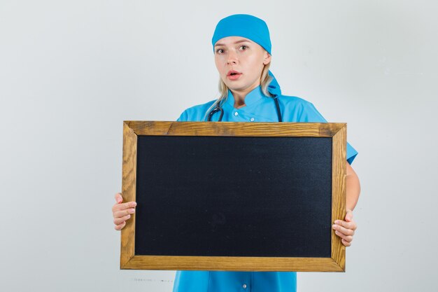 Doctora en uniforme azul sosteniendo la pizarra y mirando preocupado