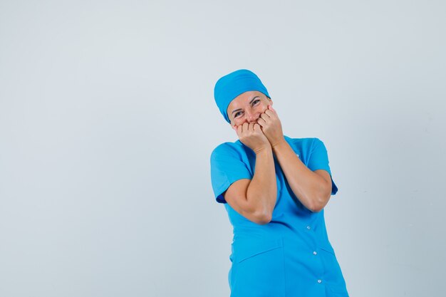 Doctora en uniforme azul sosteniendo los puños en la cara y mirando alegre, vista frontal.