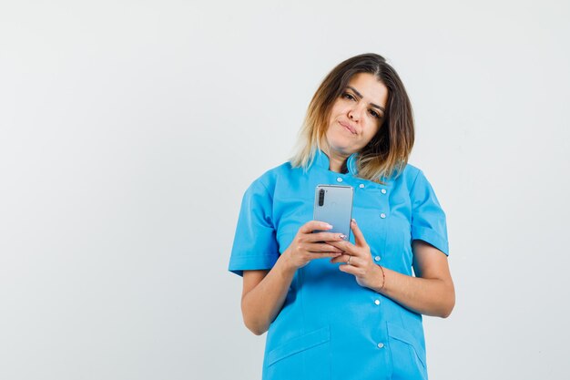 Doctora en uniforme azul sosteniendo teléfono móvil y mirando pensativo