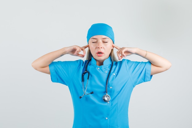 Doctora en uniforme azul tapando los oídos con los dedos y mirando molesto