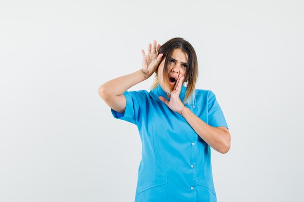 Doctora en uniforme azul tocando la cara con las manos y luciendo delicada