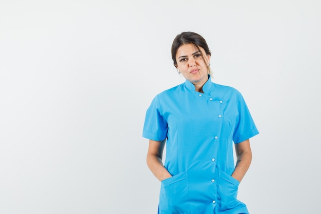 Doctora en uniforme azul tomados de la mano en los bolsillos y mirando confiado