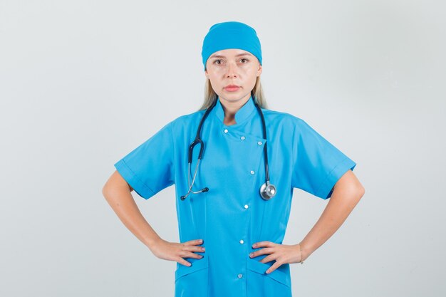 Doctora en uniforme azul tomados de la mano en la cintura y mirando serio