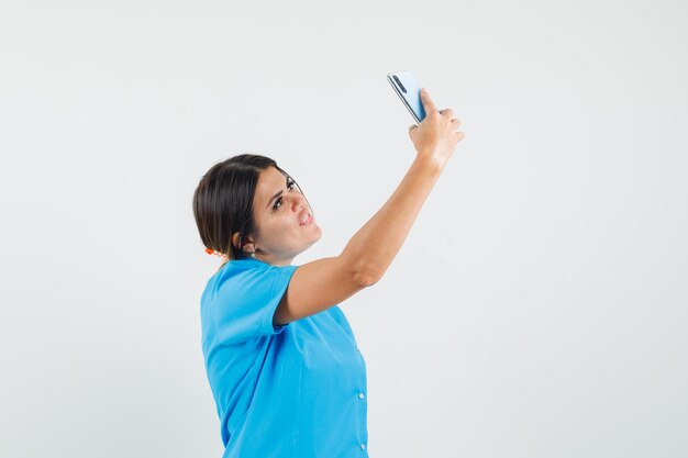 Doctora en uniforme azul tomando selfie en teléfono móvil y mirando feliz