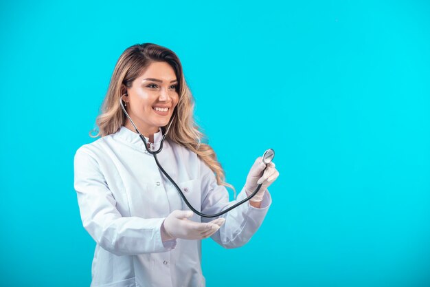 Doctora en uniforme blanco comprobando con estetoscopio y escuchando atentamente.