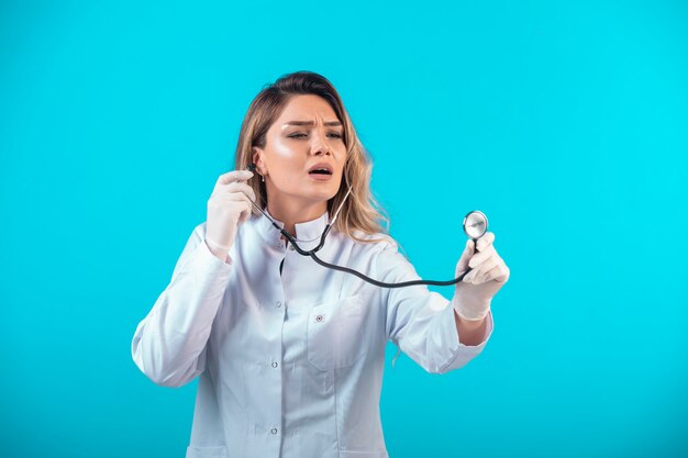 Doctora en uniforme blanco comprobando con estetoscopio y escuchando atentamente.