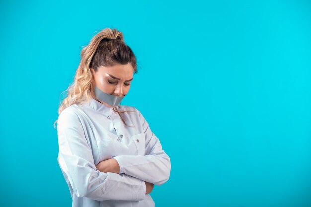 Doctora en uniforme blanco tapándose la boca y protestando.