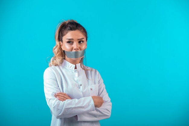 Doctora en uniforme blanco tapándose la boca y protestando.