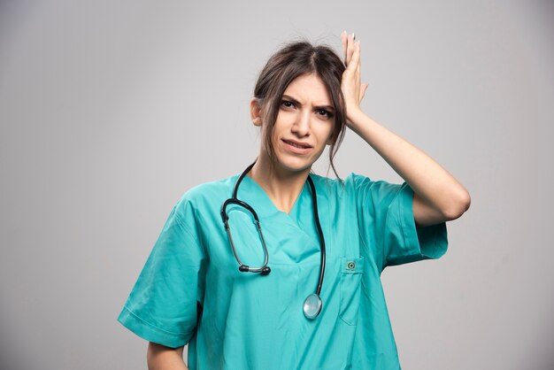 Doctora en uniforme sosteniendo su cabeza en gris