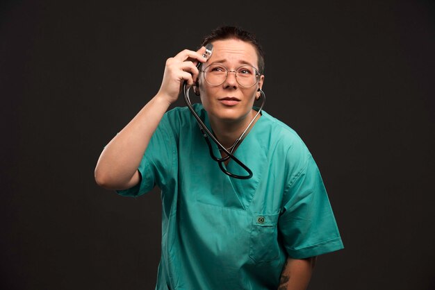 Doctora en uniforme verde sosteniendo un estetoscopio y controlándolo.