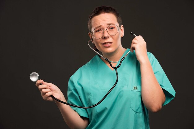 Doctora en uniforme verde sosteniendo un estetoscopio y escuchando al paciente.