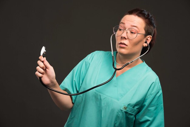 Doctora en uniforme verde sosteniendo un estetoscopio y escuchando.