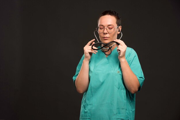 Doctora en uniforme verde sosteniendo un estetoscopio y usándolo.