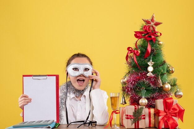 Doctora vistiendo máscara de fiesta y sosteniendo una nota de archivo en amarillo