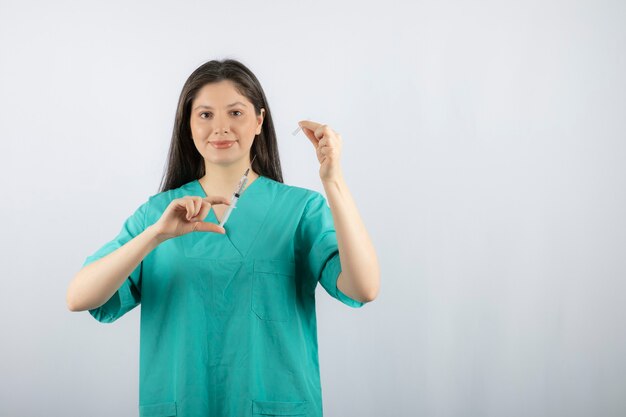 Doctora vistiendo uniforme verde con jeringa en blanco.