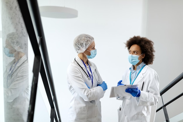 Doctoras con mascarillas discutiendo sobre los datos médicos del paciente en el vestíbulo de un hospital