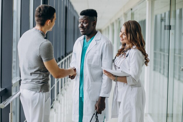 Doctores dándose la mano con el paciente, de pie en el pasillo del hospital.