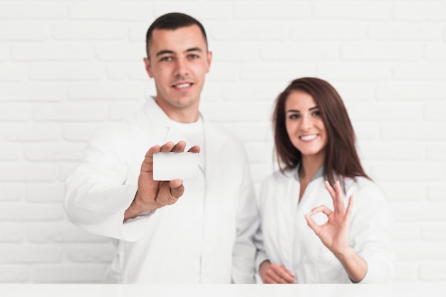 Doctores sonrientes que muestran el signo y la tarjeta de maquetas