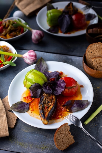 dolma con carne picada tomates pimiento verde y hojas moradas dentro de un plato blanco