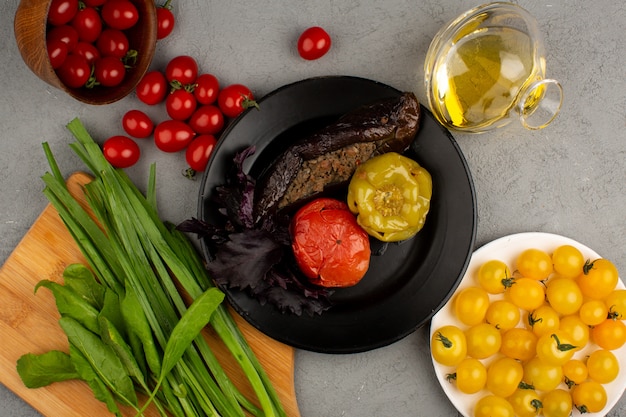 Dolma famosa comida de carne del este dentro de un plato negro junto con tomates frescos amarillos y rojos maduros y aceite de oliva