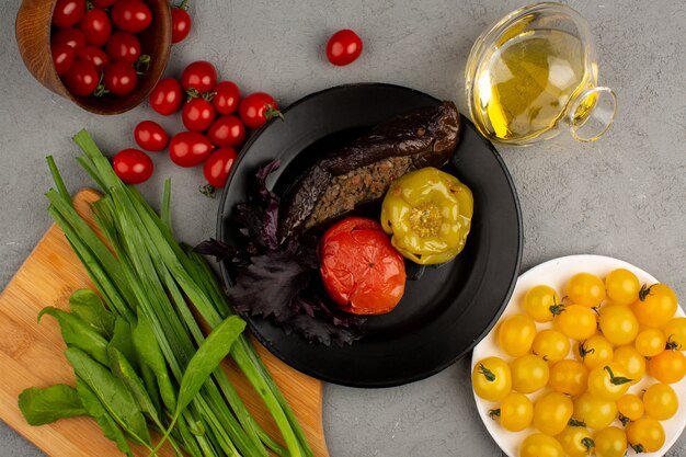 Dolma famosa comida de carne del este dentro de un plato negro junto con tomates frescos amarillos y rojos maduros y aceite de oliva