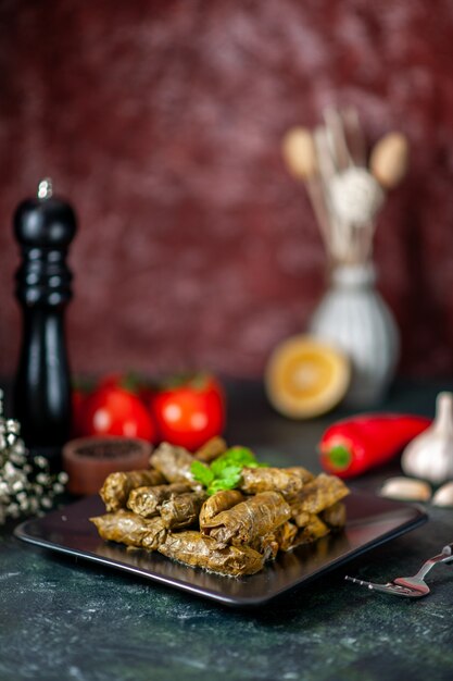 Dolma de hoja deliciosa vista frontal con tomates rojos sobre fondo oscuro