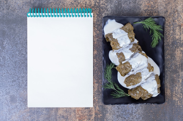 Foto gratuito dolma de hojas de parra rellenas en placa con yogur y cuaderno.