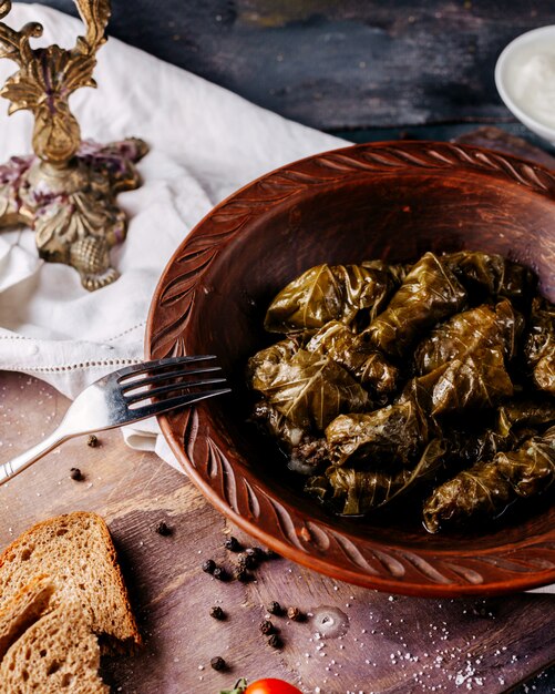 Dolma verde sabrosa carne salada rellena dentro de un plato redondo marrón en la superficie gris