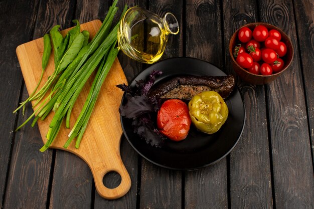 Dolma de verduras dolma con carne picada en el interior con aceite de oliva verde y tomates rojos en el escritorio de madera rústica