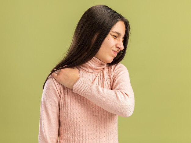 Dolor bastante adolescente de pie en la vista de perfil manteniendo la mano sobre el hombro con los ojos cerrados aislado en la pared verde oliva con espacio de copia