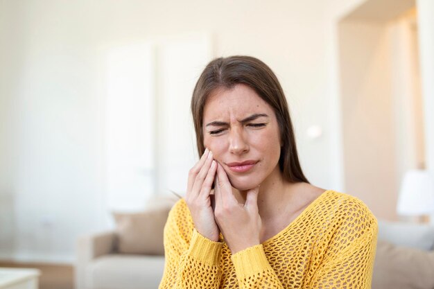 Dolor de dientes y odontología Hermosa mujer joven que sufre de terrible dolor de dientes fuertes Tocar la mejilla con la mano Mujer Sentir dolor de muelas Dolor dental Cuidado dental y concepto de salud Alta resolución