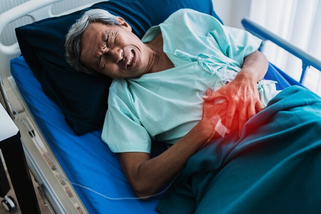 Dolor y estómago viejo abuelo asiático senior en uniforme de paciente sufren de problemas corporales concepto de ideas de salud