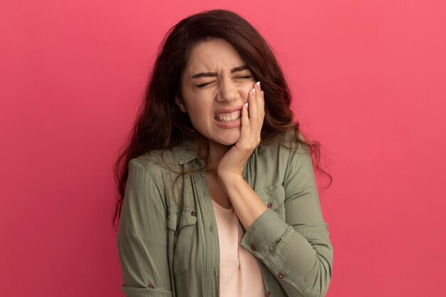 Dolor joven hermosa chica vistiendo camiseta verde oliva poniendo la mano sobre el dolor de muelas aislado en la pared rosa