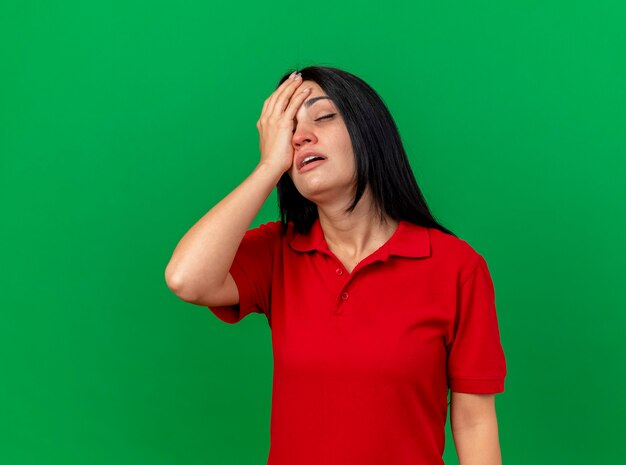 Dolor de niña enferma caucásica joven poniendo la mano en la cabeza con los ojos cerrados aislado en la pared verde con espacio de copia