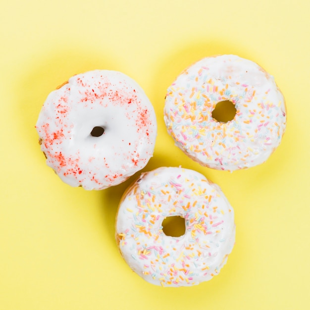 Foto gratuita donas dulces glaseadas con chispas sobre fondo amarillo