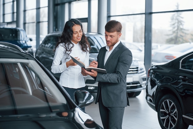 Donde necesito firmar. Clienta y empresario barbudo con estilo moderno en el salón del automóvil