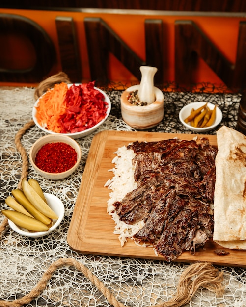 Doner kebab de cordero colocado sobre arroz cubierto con pan plano servido con pepinillos y pimienta