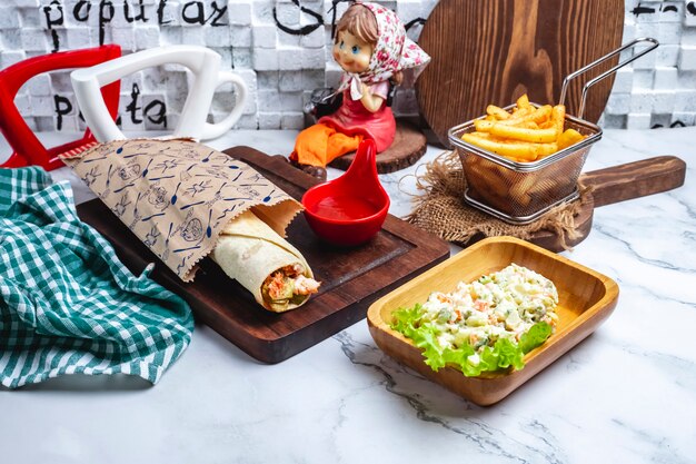 Doner en pan de pita con salsa de tomate en un tablero con papas fritas y una ensalada en la capital