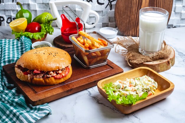 Doner de pollo en pan con papas fritas en un tablero una ensalada capital y un vaso de yogurt