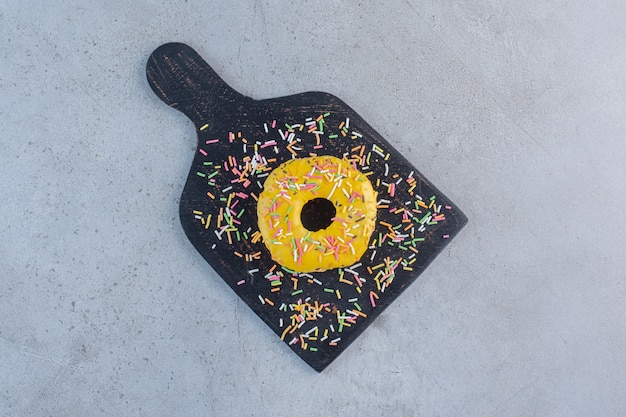 Donut amarillo único decorado con chispitas en la tabla de cortar.