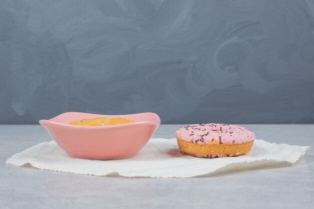 Donut con aspersores y tazón de torta en la mesa de mármol.