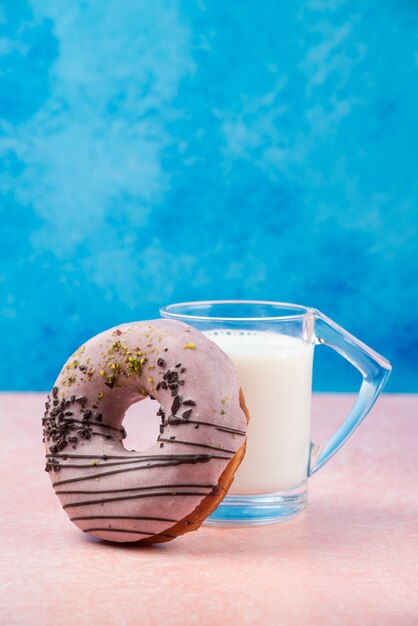 Donut de fresa con adornos y un vaso de leche en la mesa rosa.