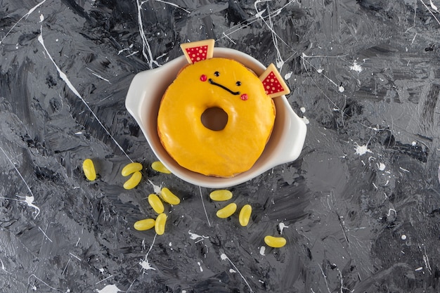 Foto gratuita donut glaseado amarillo con caramelos de frijoles colocados sobre una mesa de mármol.