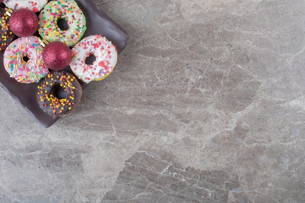 Donuts y adornos navideños dispuestos en una bandeja sobre la superficie de mármol