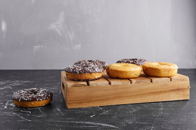 Donuts de chocolate sobre una superficie negra en una bandeja de madera.