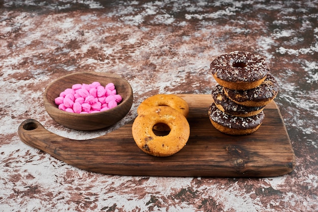 Donuts de chocolate sobre una tabla de madera con caramelos de color rosa.