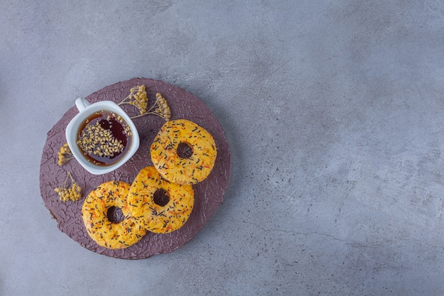 Donuts dulces amarillos y taza de té de hierbas en la pieza de madera.