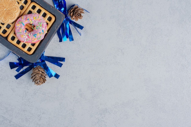 Foto gratuita donuts, galletas y una mermelada en una pequeña bandeja en medio de piñas sobre una superficie de mármol