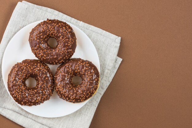Donuts glaseados chocolate en plato blanco sobre tela gris