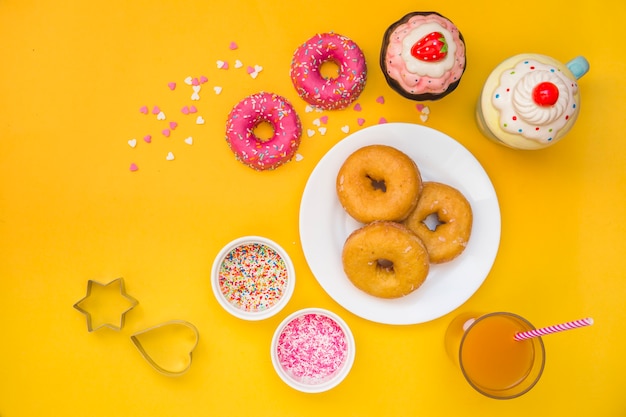 Donuts, jugo, magdalenas y cortador de pastelería sobre fondo amarillo